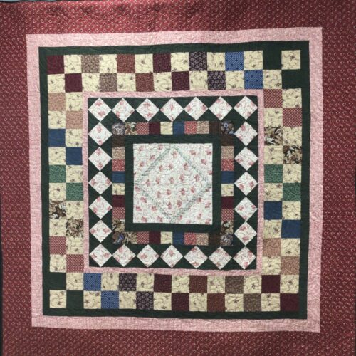 Full bed medallion quilt with floral center surrounded by diamond border, checkerboard, and multiple frames in burgundy, green, and pink