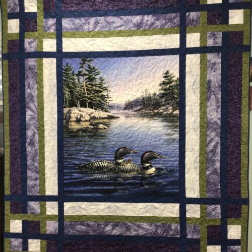 Twin bed quilt with loon panel showing loons on lake with pine trees, framed by pieced borders in navy, green, purple, and white