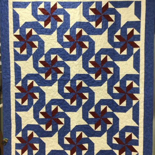 Twin bed quilt with spinning pinwheel blocks in burgundy red and royal blue on white background