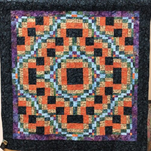 Throw quilt with bargello-style interlocking blocks in orange, black, tan, aqua, and green batiks with purple inner border and black outer border