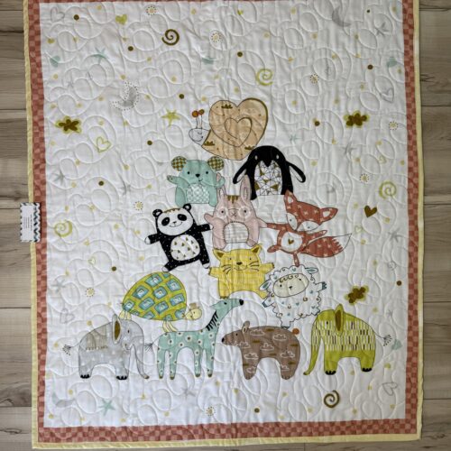 Handmade panel baby quilt with whimsical stacked animal characters including elephant, panda, fox, bunny, and turtle on a white background scattered with moons, stars, and hearts with a pink checkered border.