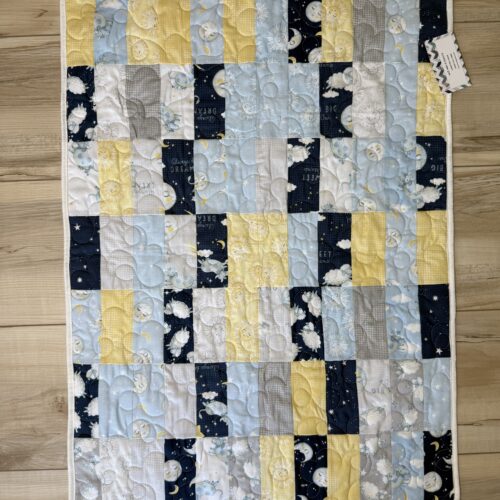 Handmade baby quilt in navy, light blue, yellow, and gray patchwork featuring sheep, cows, moons, suns, and stars with sweet dreams text.