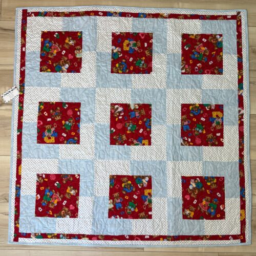 Handmade baby quilt with nine red teddy bear print blocks framed in light blue and white polka dot fabric, pieced in the Town Square pattern from Fabric Cafe.
