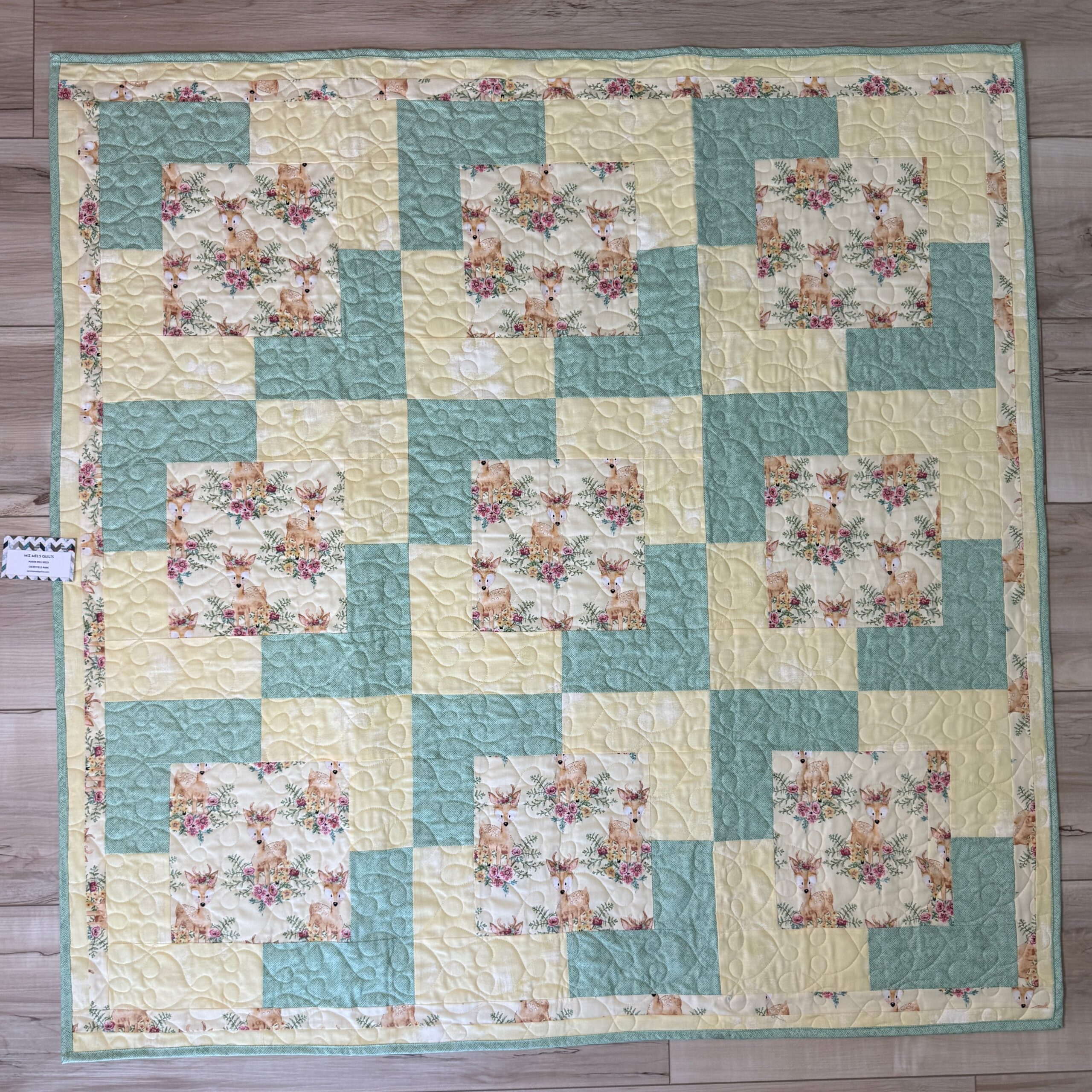Handmade baby quilt with fawn and floral print blocks framed in soft mint green and pale yellow, pieced in the Town Square pattern from Fabric Cafe