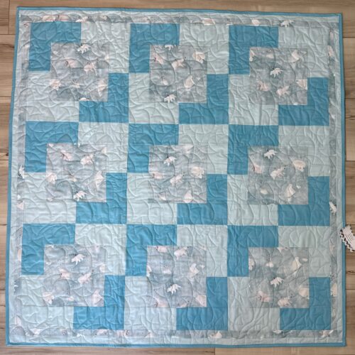 Handmade baby quilt in blue and teal patchwork with polar bear family prints, featuring adult and baby bears on a snowy gray background.