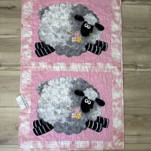 Handmade pink baby quilt featuring two large sheep with curly fleece, holding flowers, on a pink polka dot background.