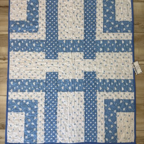 Handmade baby quilt in blue and white woven strip piecing with small heart, kite, and cloud prints, backed with a colorful sailboat print.