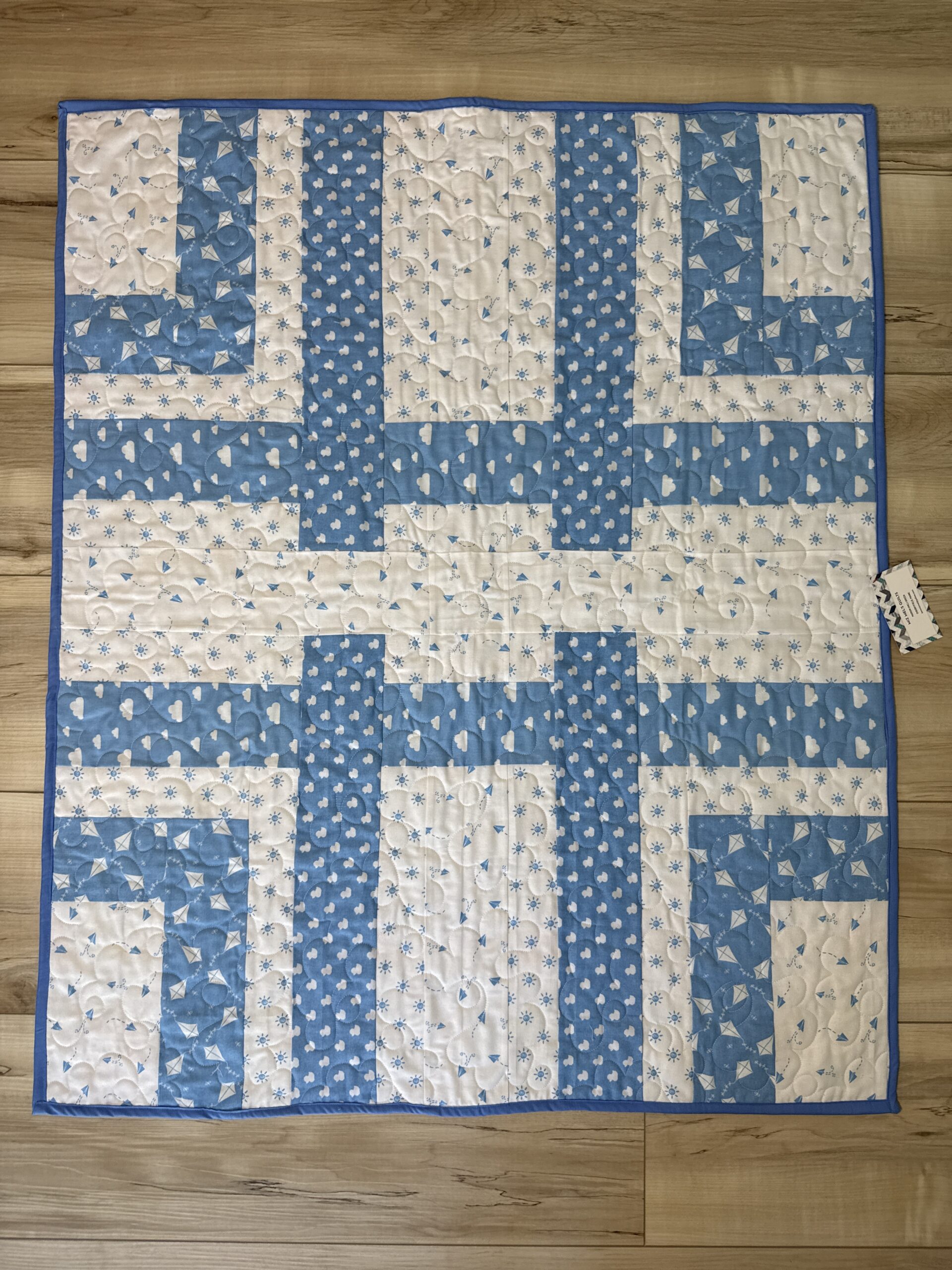 Handmade baby quilt in blue and white woven strip piecing with small heart, kite, and cloud prints, backed with a colorful sailboat print.