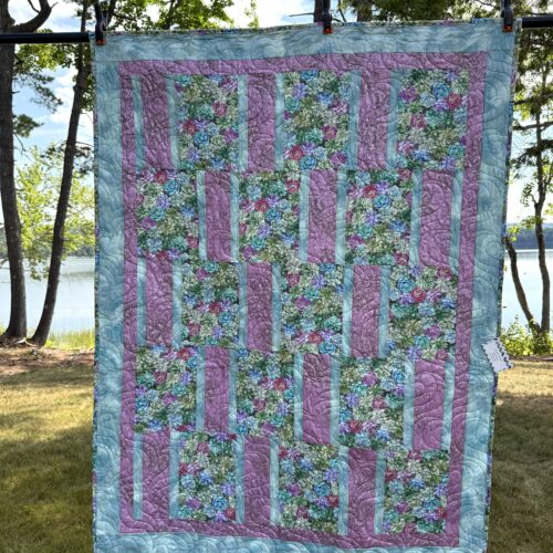 Handmade lap quilt with realistic succulent print blocks in green, teal, pink, and magenta, alternating with rose pink and pale teal strips, framed by a pink inner border and wide teal outer border.