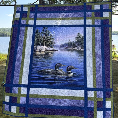 Twin bed quilt with loon panel showing loons on lake with pine trees, framed by pieced borders in navy, green, purple, and white