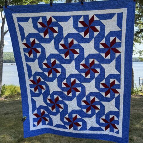 Twin bed quilt with spinning pinwheel blocks in burgundy red and royal blue on white background