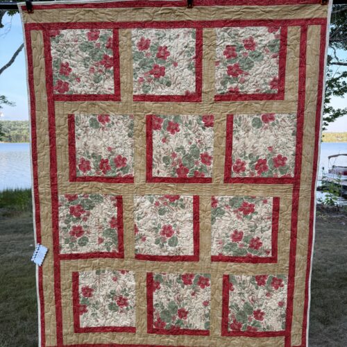 Handmade lap quilt with twelve large red floral print blocks on cream, framed in dark red and gold sashing, pieced in the Bold Blocks pattern by Fabric Cafรฉ.