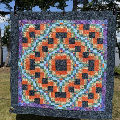 Throw quilt with bargello-style interlocking blocks in orange, black, tan, aqua, and green batiks with purple inner border and black outer border