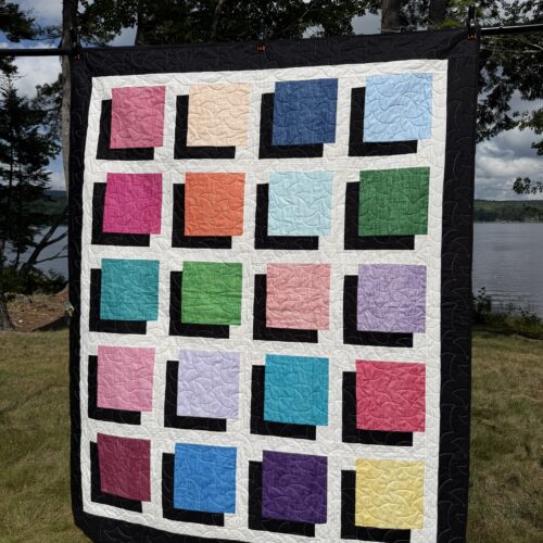 Throw quilt with shadow box pattern creating 3D illusion using colored squares with black shadows on white background and black border