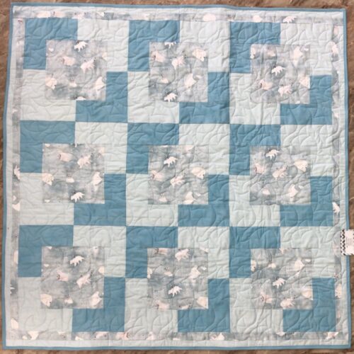 Handmade baby quilt in blue and teal patchwork with polar bear family prints, featuring adult and baby bears on a snowy gray background.