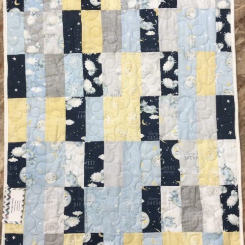 Handmade baby quilt in navy, light blue, yellow, and gray patchwork featuring sheep, cows, moons, suns, and stars with sweet dreams text.