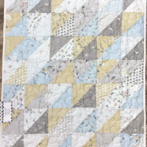Handmade baby quilt with half-square triangle patchwork in soft yellow, light blue, gray, and white nursery prints featuring moons, clouds, and botanical motifs.