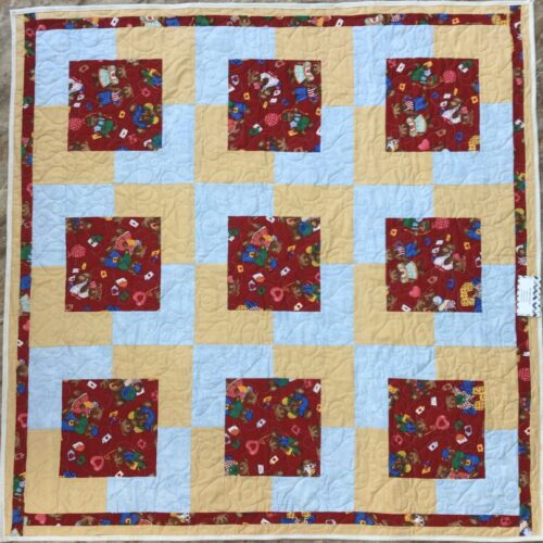 Handmade baby quilt with nine red teddy bear print blocks framed in golden yellow and light blue fabric, pieced in the Town Square pattern by Fabric Cafe.
