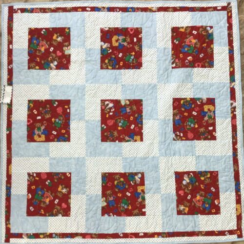 Handmade baby quilt with nine red teddy bear print blocks framed in light blue and white polka dot fabric, pieced in the Town Square pattern from Fabric Cafe.